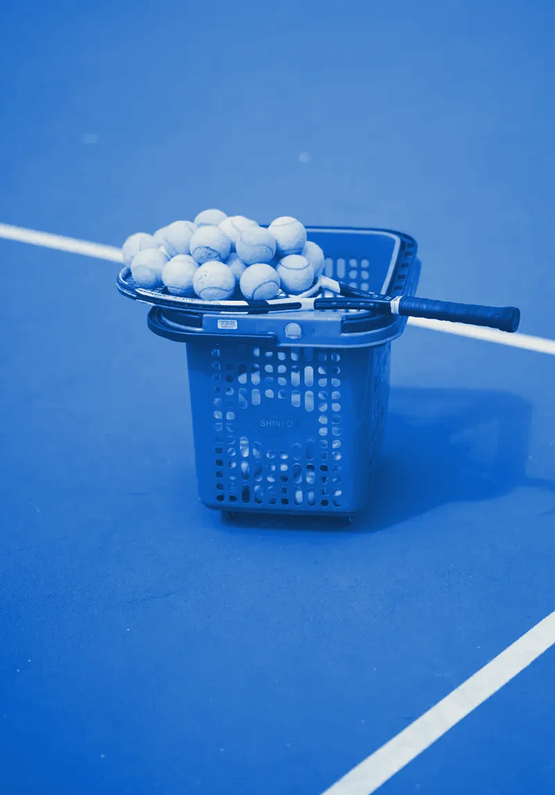 A basket of tennis balls and a racquet on a court