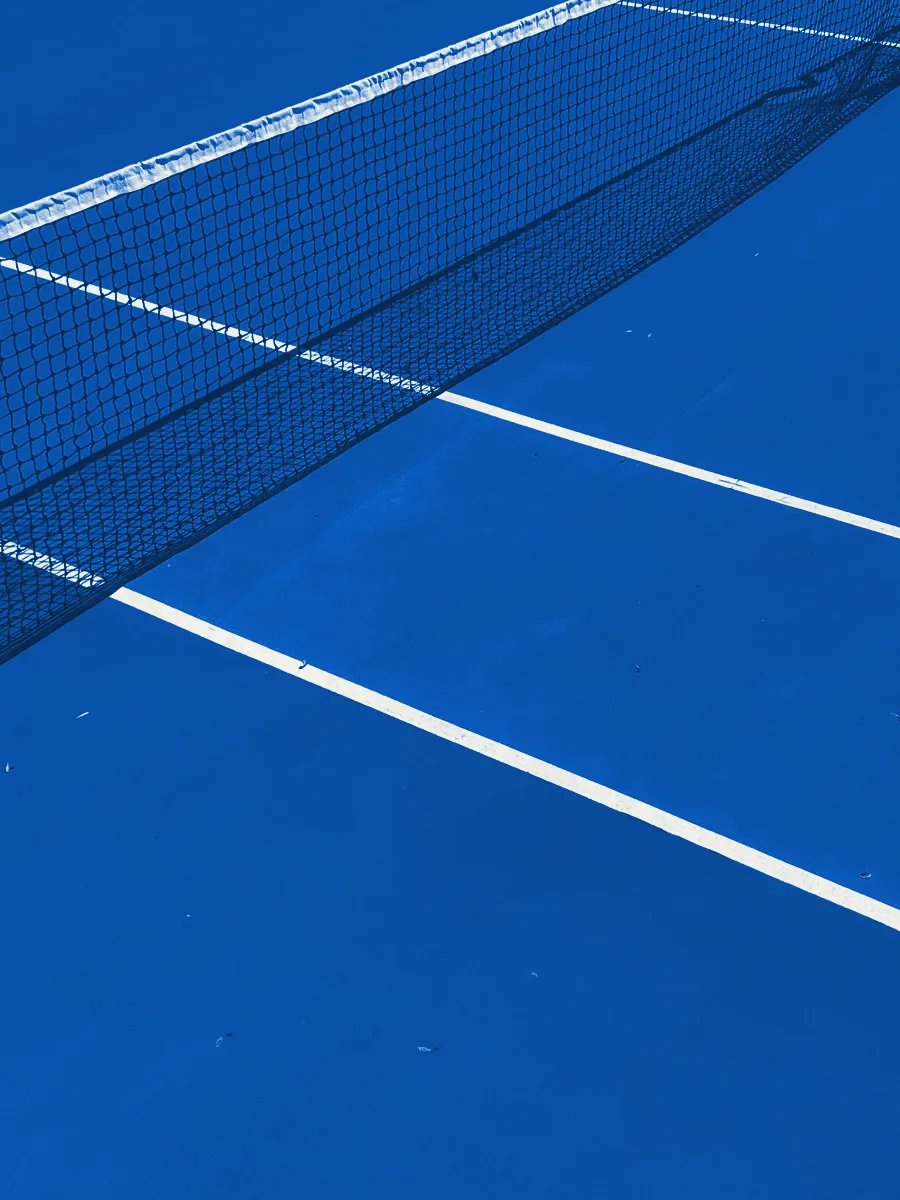 A tennis net over the line between two court surfaces